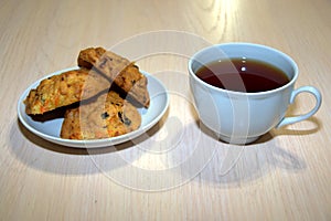 A cup of black tea and three pieces of homemade raisin cookies are on a white porcelain saucer