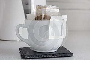 A cup of brewed natural coffee in a drip bag on the background of a teapott close-up