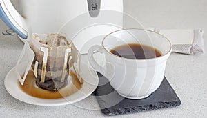 A cup of brewed natural coffee from a dropper bag on the background of a teapot close-up
