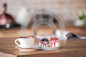 Cup and cakes on a plate stand on the table on blurred background of the kitchen interior