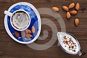 Cup of cappuccino almonds and milk in a glass milk jug on a dark wooden table