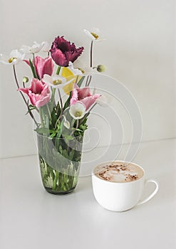 A cup of cappuccino and a bouquet of spring garden flowers on the table. Cozy slow morning