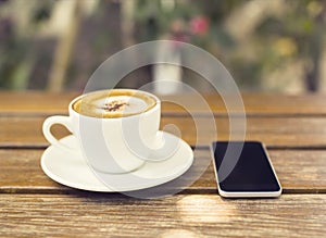 Cup of cappuccino and cell phone on a wooden table