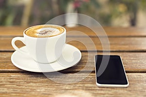 Cup of cappuccino and a cell phone on a wooden table