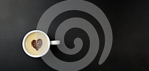 Cup of cappuccino in the center of the heart, on a black background with copy space. Chocolate heart in a cup with a hot coffee