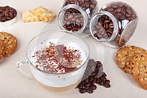Cup of cappuccino with chocolate crumbs, cookies, crackers and coffee beans on table