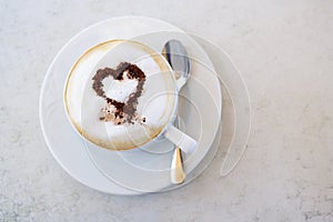 Cup of cappuccino with cocoa powder in heart shape on a table in a street cafe, high angle view from above, copy space