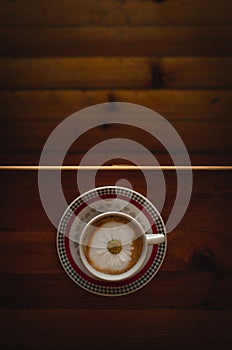 Cup of cappuccino coffee and croissant / brioche on a wooden table with freshly gathered daisy flowers. Italian breakfast.