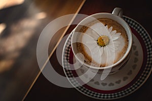 Cup of cappuccino coffee and croissant / brioche on a wooden table with freshly gathered daisy flowers. Italian breakfast.