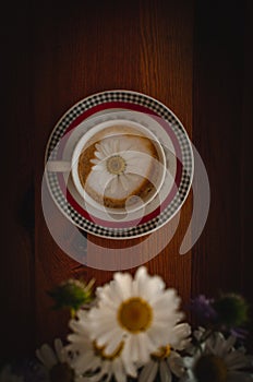 Cup of cappuccino coffee and croissant / brioche on a wooden table with freshly gathered daisy flowers. Italian breakfast.