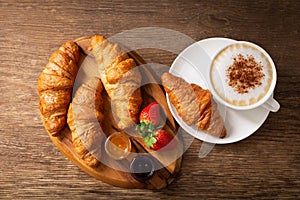 Cup of cappuccino coffee, jam, strawberries and croissant, top view
