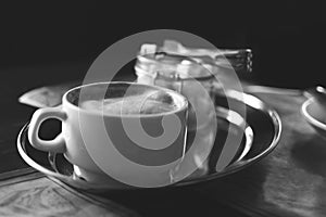 A cup of cappuccino coffee and sugar in a glass vase on a table in a cafe. Black and white photography