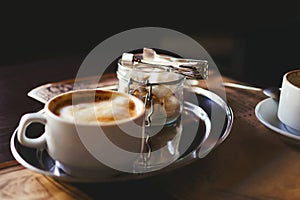 A cup of cappuccino coffee and sugar in a glass vase on a table in a cafe. Toning style instagram