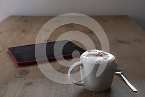 Cup of cappuccino coffee and a tablet on a rustic  table