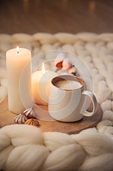 Cup of cappuccino, cookies, and candles on the background of blanket of thick yarn