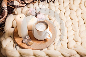 Cup of cappuccino and cookies, candles, checkered plaid on the background of blanket of thick yarn