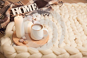 Cup of cappuccino and cookies, candles, checkered plaid, inscription Home on the background of blanket of thick yarn