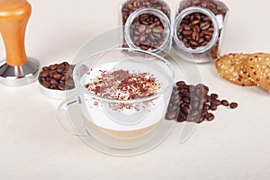 Cup of cappuccino, cookies, coffee beans and tamper on table