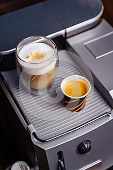 Cup of cappuccino and a cup of espresso are standing on top of an office coffee machine. Inexpensive  simple coffee machine model