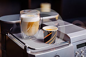 Cup of cappuccino and a cup of espresso are standing on top of an office coffee machine. Inexpensive  simple coffee machine model