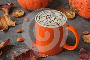 A cup of cappuccino with ghosts, spiderweb on dark stone table with pumpkins, maple leaves. Fall time, Halloween concept