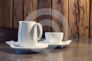 Cup of cappuccino and jug of milk on wooden background.