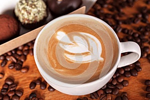 Cup of cappuccino with latte-art and cakes on a wooden table with scattered coffee beans. Presentation of coffee