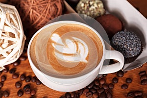 Cup of cappuccino with latte-art and cakes on a wooden table with scattered coffee beans. Presentation of coffee