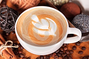 Cup of cappuccino with latte-art and cakes on a wooden table with scattered coffee beans. Presentation of coffee