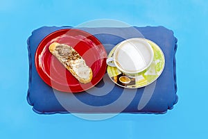 A cup of cappuccino and a red plate with a slice of bread spread with black and white chocolate cream