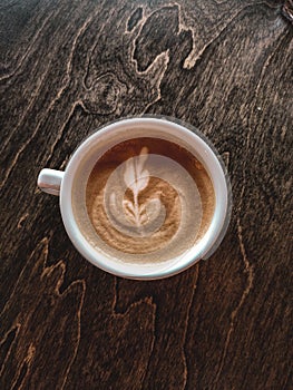 A cup of cappuccino on a table in a cafe. Beautiful plant drawing Leaf on Latte coffee froth. View from above. Flat lay. Delicious