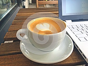 Cup of cappuccino and white laptop on wooden cafe table