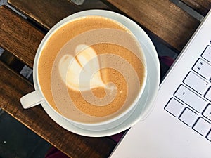 Cup of cappuccino and white laptop on wooden cafe table