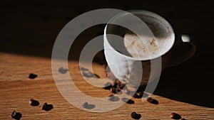 Cup of cappuccino on a wooden table, coffee beans fall on the table in slow motion