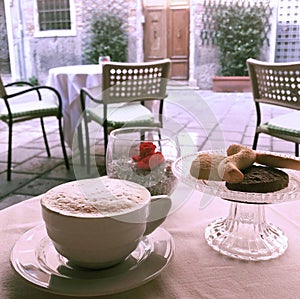 A cup of capuccino coffee on an outside cafe table with a view of a quiet Venice street