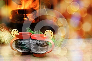 Cup with Christmas ornament near fireplace. Mug in knitted cloth