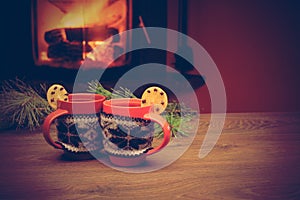 Cup with Christmas ornament near fireplace. Mug in knitted cloth