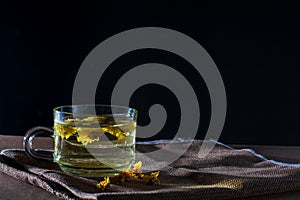 Cup of Chrysanthemum tea with dry flower on brown table cloth on black background. Healthy beverrage for drink. Herbs and medical