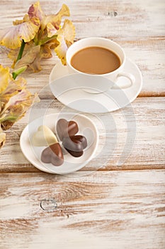 Cup of cioffee with chocolate candies, lilac and purple iris flowers on white wooden background. side view, close up