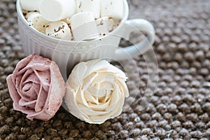 A cup of cocoa or chocolate next to a rose-shaped marshmallow. Warm cozy square background