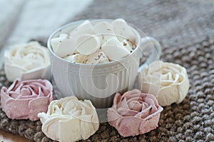 A cup of cocoa or chocolate next to a rose-shaped marshmallow. Warm cozy square background