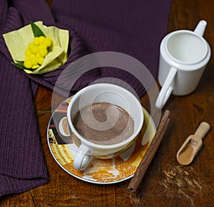 A cup of cocoa and cinnamon milk with cinnamon powder and stick on a wooden table