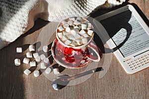 A cup of cocoa on an grey wooden background with a spoon and reader, marshmelow