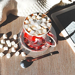 A cup of cocoa on an grey wooden background with a spoon and reader, marshmelow