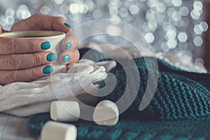 A cup of cocoa with marshmallow in female hands with a blue manicure on a shiny background