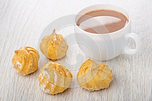 Cup of cocoa with milk, profiterole in sugar powder on table