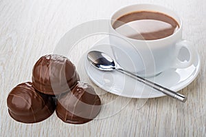 Cup of cocoa with milk, spoon on saucer, chocolate desserts with