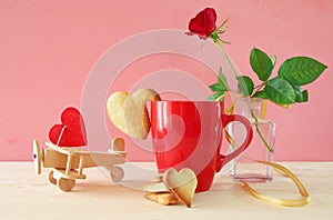 Cup of coffe with cookies next to one red rose in the vase