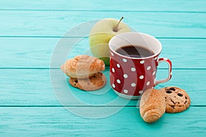 Cup of coffee, apple fruit with croissants on blue wooden table. Selective focus. Copy space