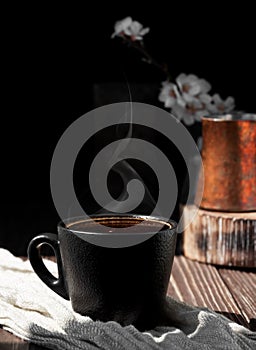 Cup of coffee of aromatic espresso on a wooden background, close-up. Steam rises over hot coffee. Vertical frame, copy space.